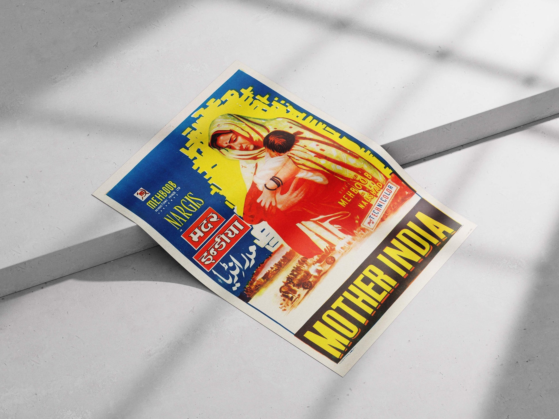 Vintage movie poster for 'Mother India' on a gray surface Vibrant blue and yellow Mother India movie poster with Nargis holding a child, styled in a modern minimalist bedroom.