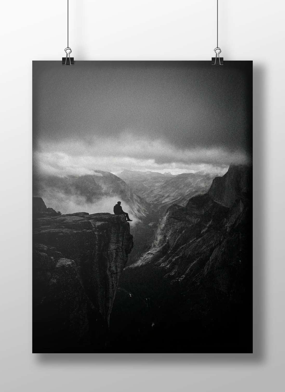 A solitary man seated on a rocky cliff edge overlooking a mountainous valley Main Subject: A solitary man seated on a rocky