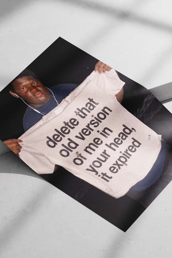 The phrase "delete that old version of me in your head, it expired" printed on a T-shirt. Main Subject: The phrase "delete
